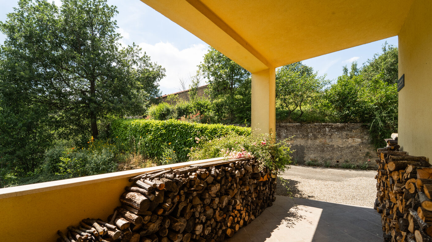Log store beneath the covered terrace, with the garden and courtyard beyond