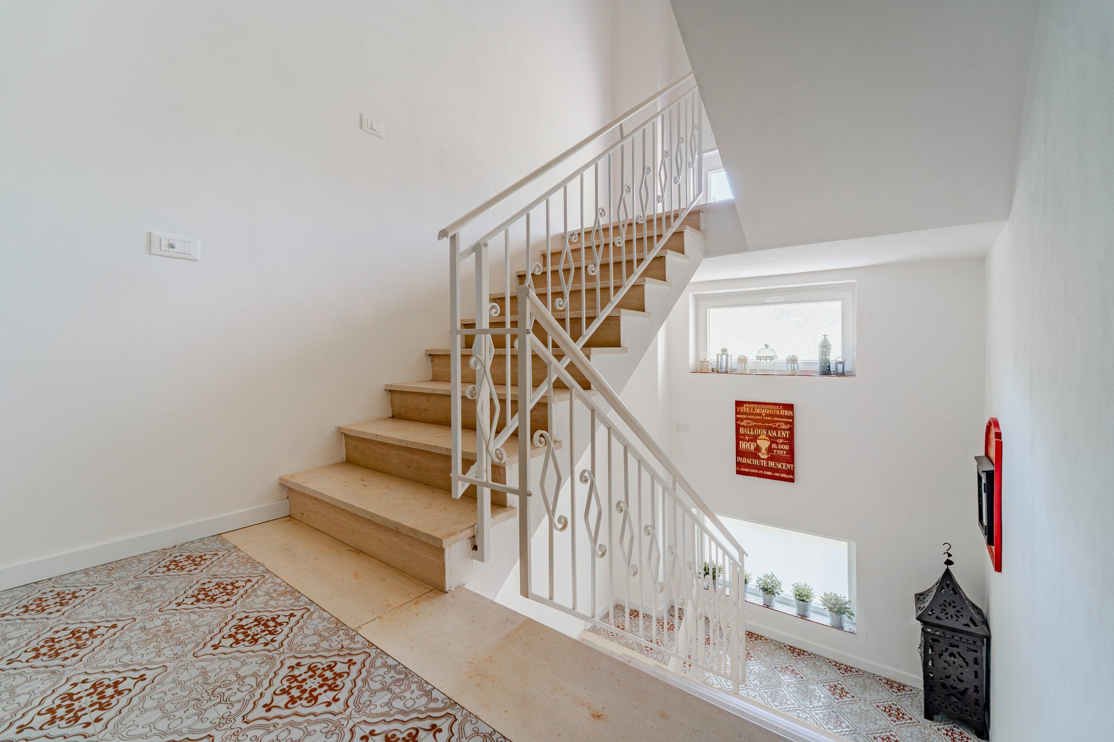 Bright stairwell with original patterned ceramic tiles and white iron railings