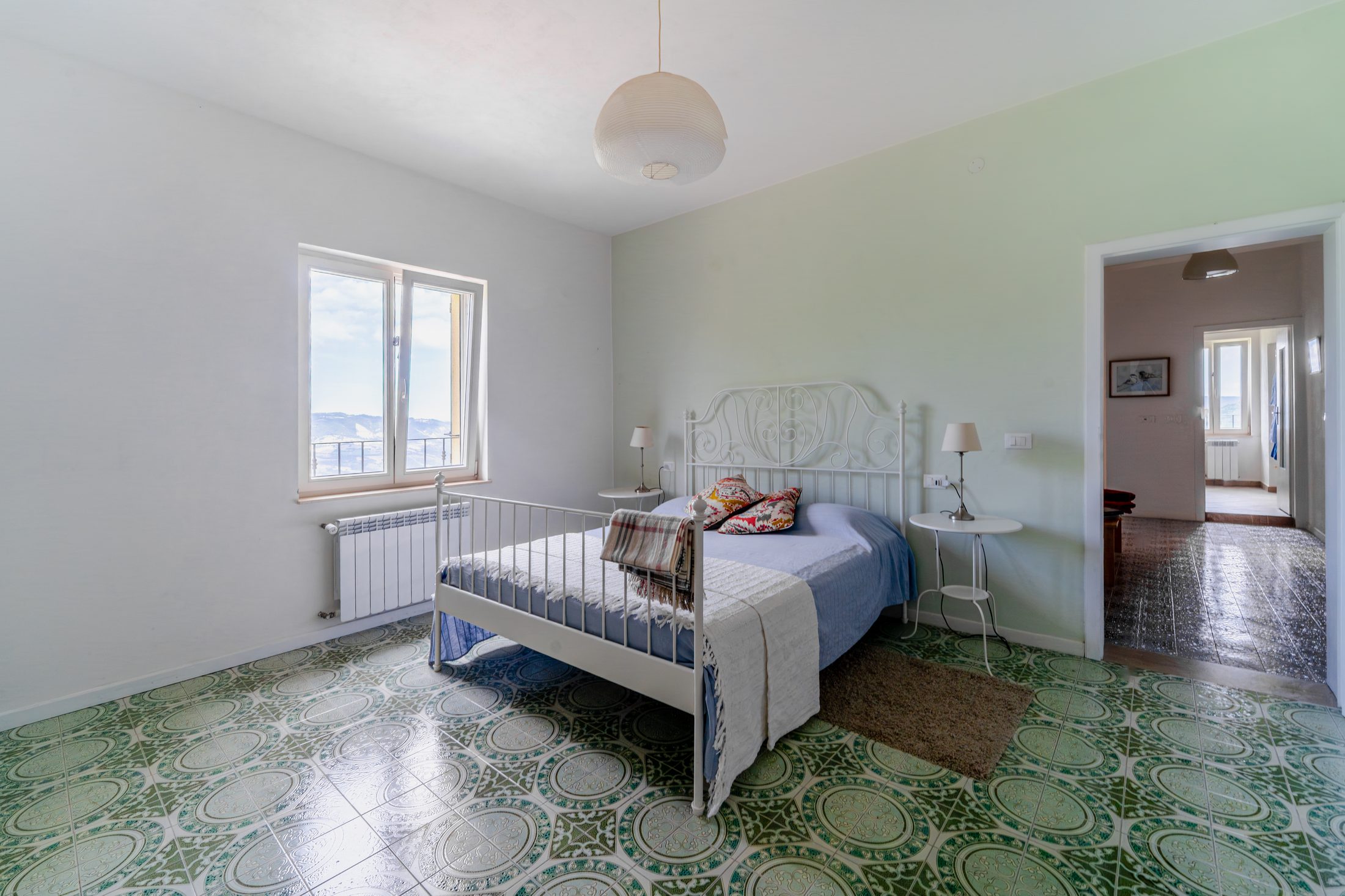 Apartment bedroom with iron bed and patterned tile floor