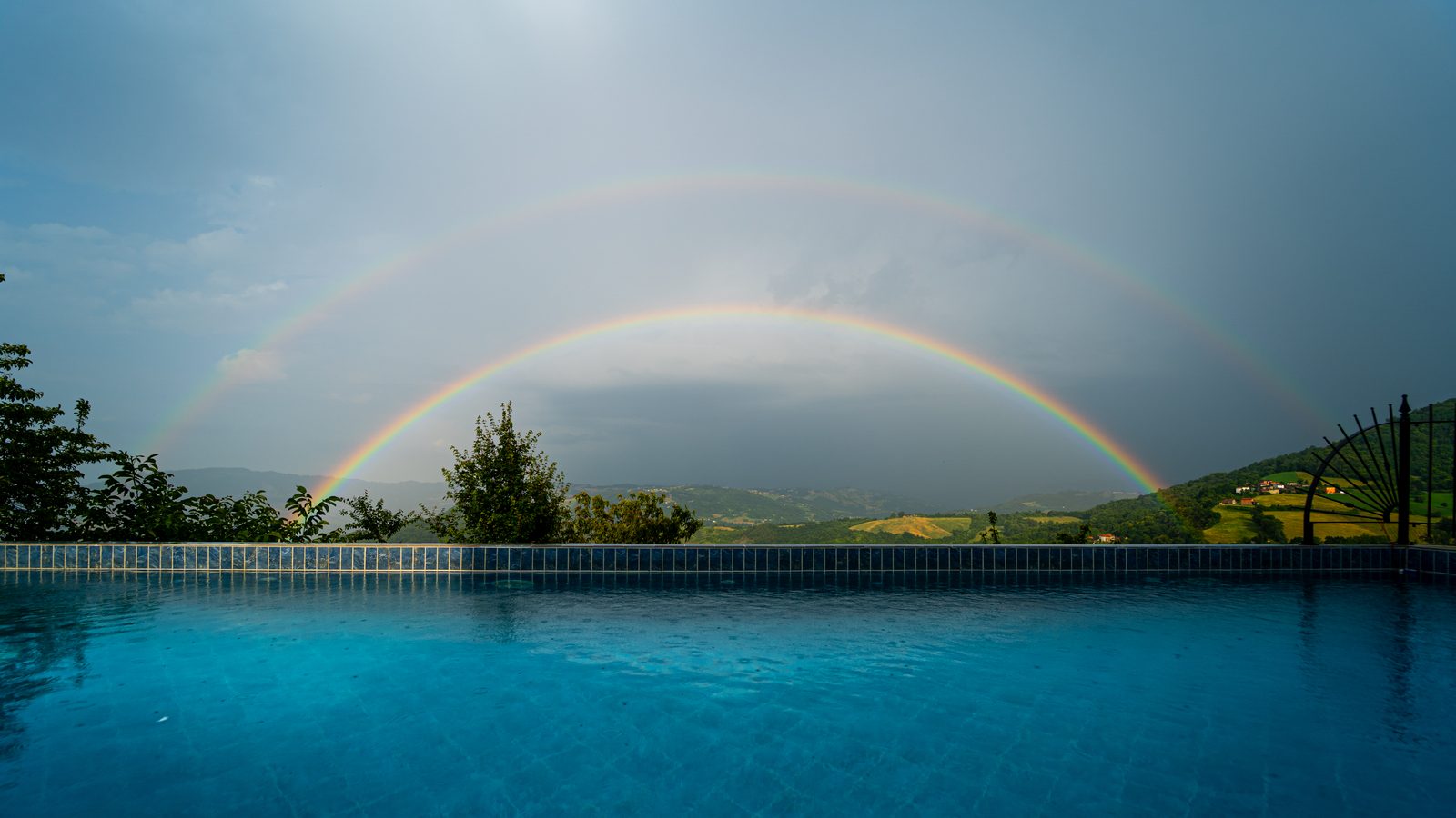 A double rainbow arcing over the pool after a summer storm