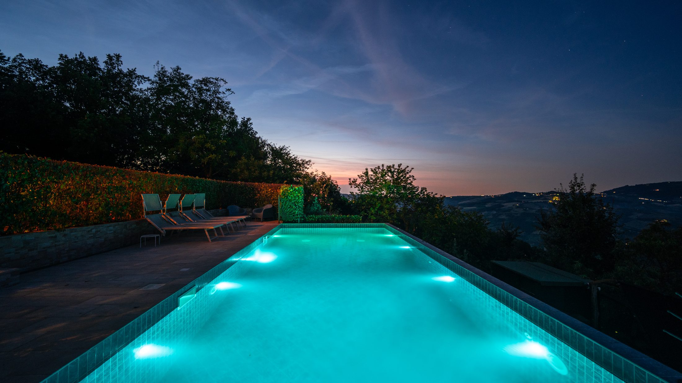 Loungers beside the glowing pool at dusk