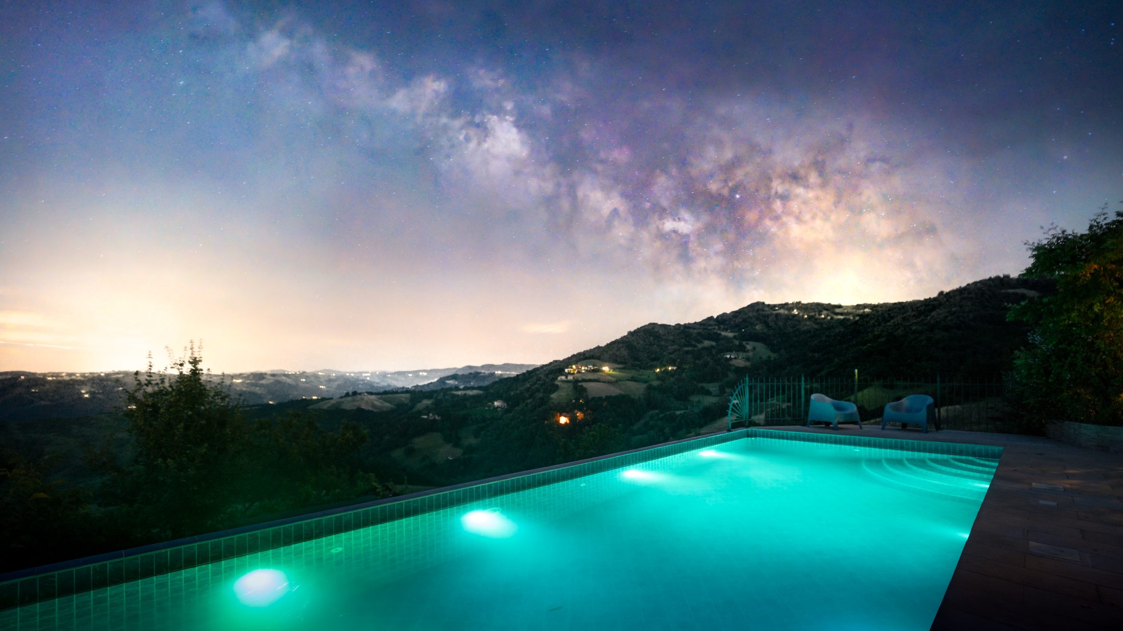 The pool lit turquoise at night, with the Milky Way overhead