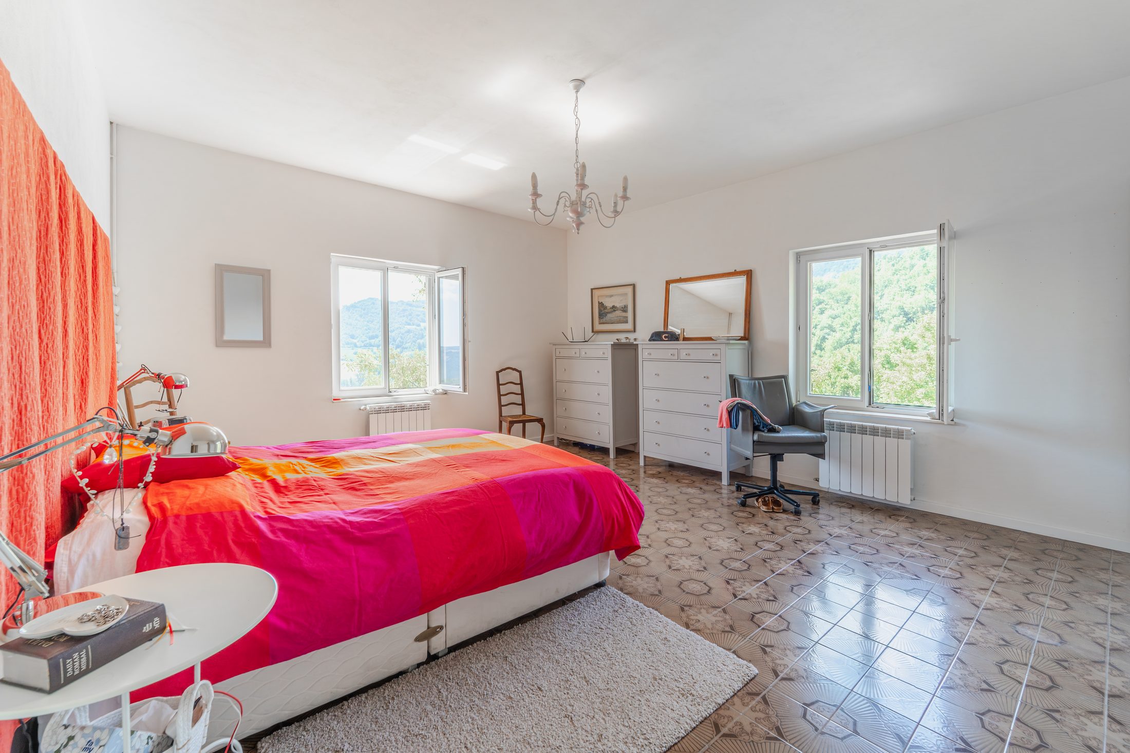 Double-aspect bedroom with orange bedspread and chandelier